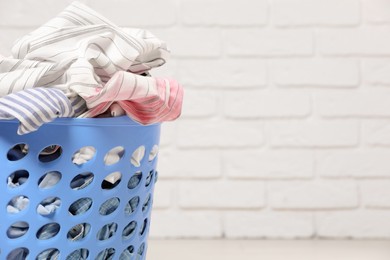 Photo of Laundry basket with clothes near white brick wall. Space for text