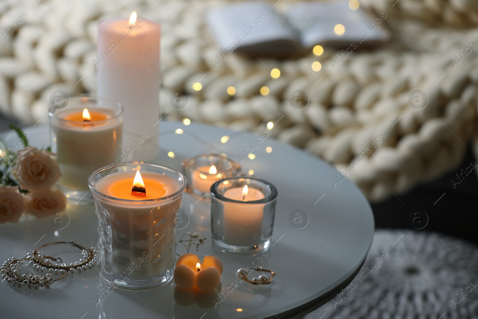 Photo of Burning candles, flowers and jewelry on table in room