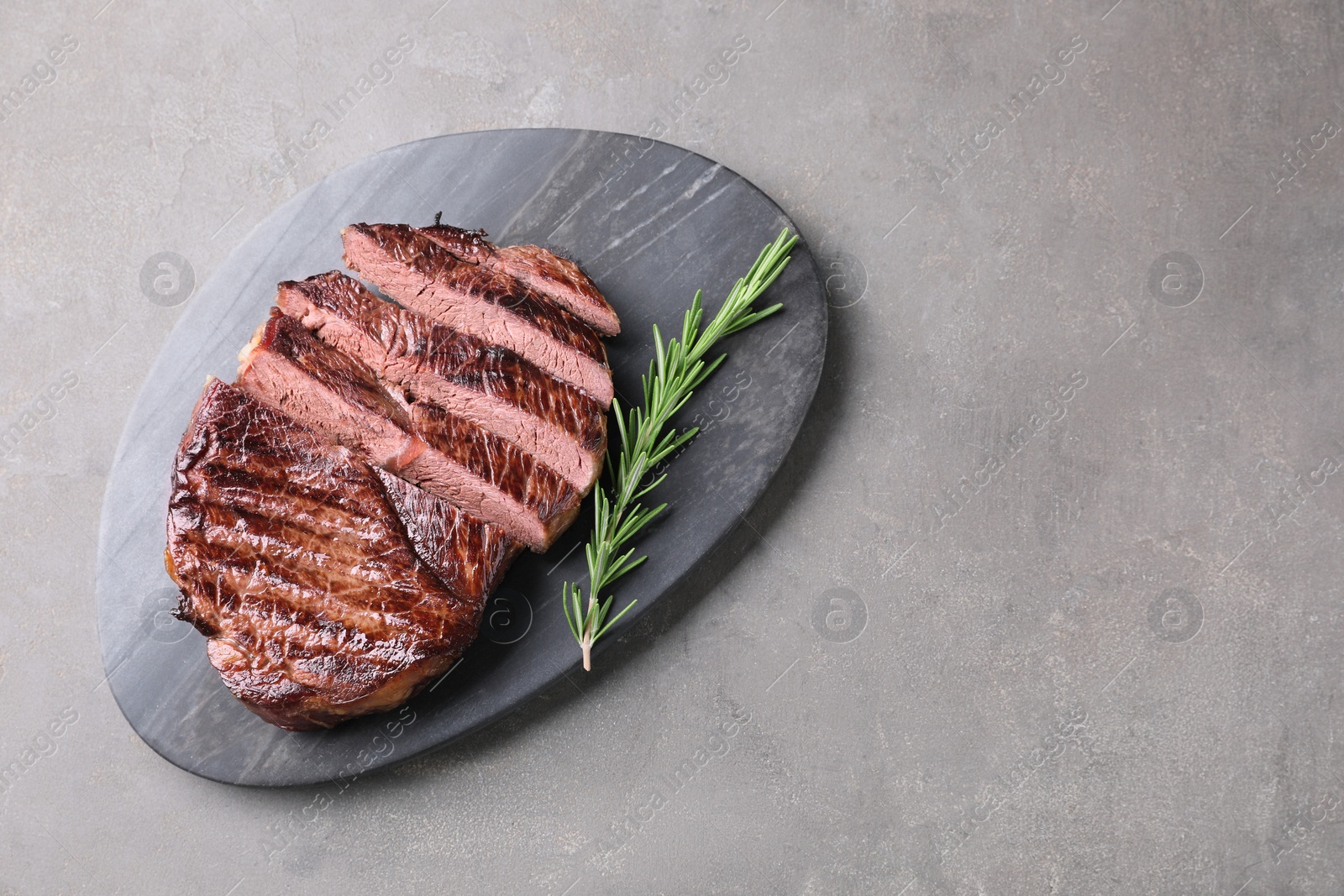 Photo of Delicious fried beef meat with rosemary on grey textured table, top view. Space for text