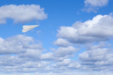 Image of White paper plane flying in blue sky with clouds