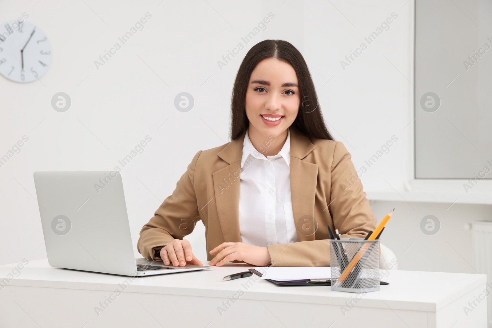 Photo of Young female intern working with laptop at table in office