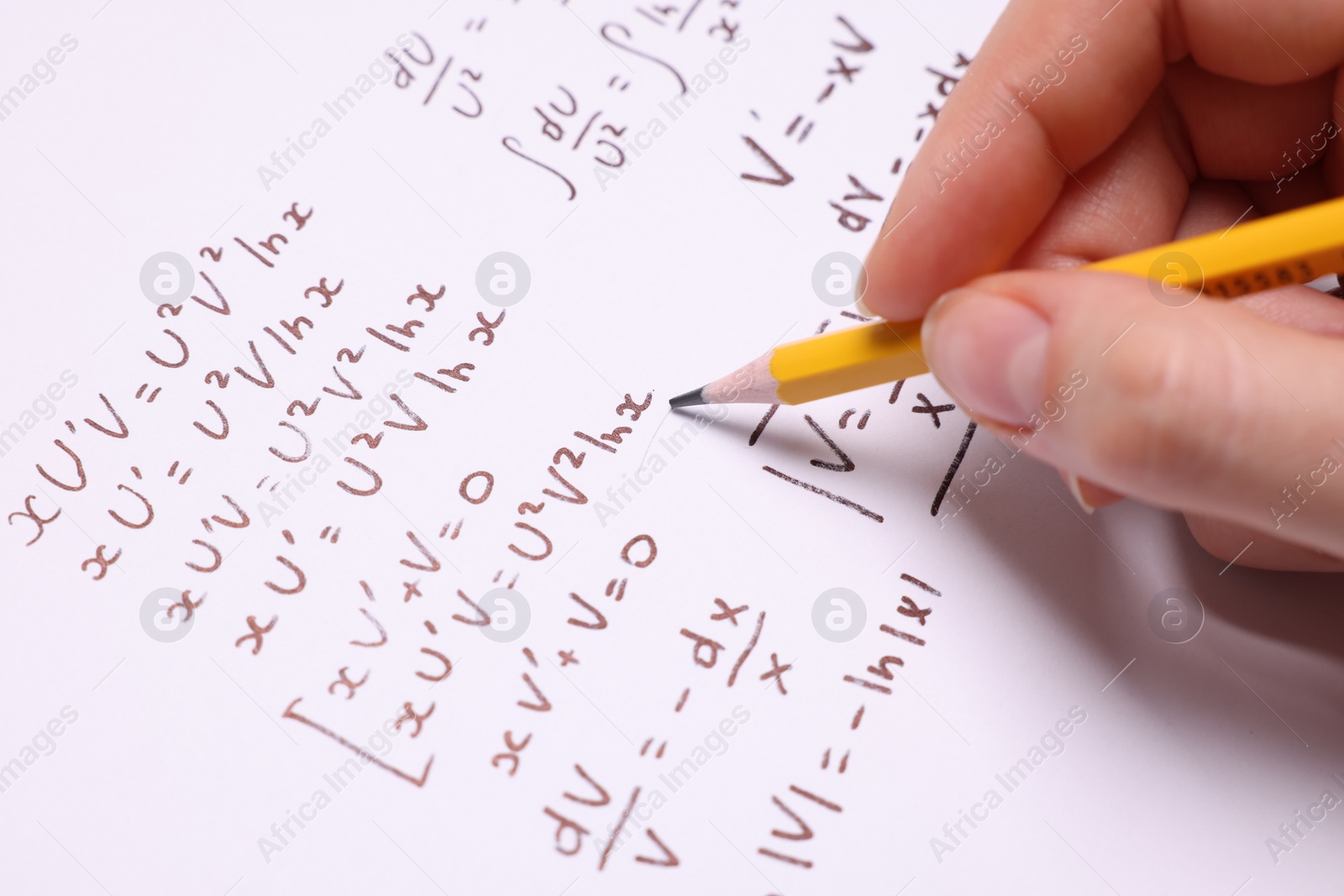 Photo of Student writing different mathematical formulas on paper, closeup