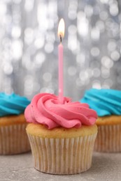 Photo of Delicious cupcakes with bright cream and burning candle on grey table, closeup