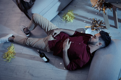 Young man sleeping in messy room after party, above view