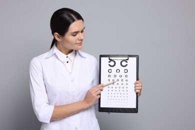Ophthalmologist pointing at vision test chart on gray background