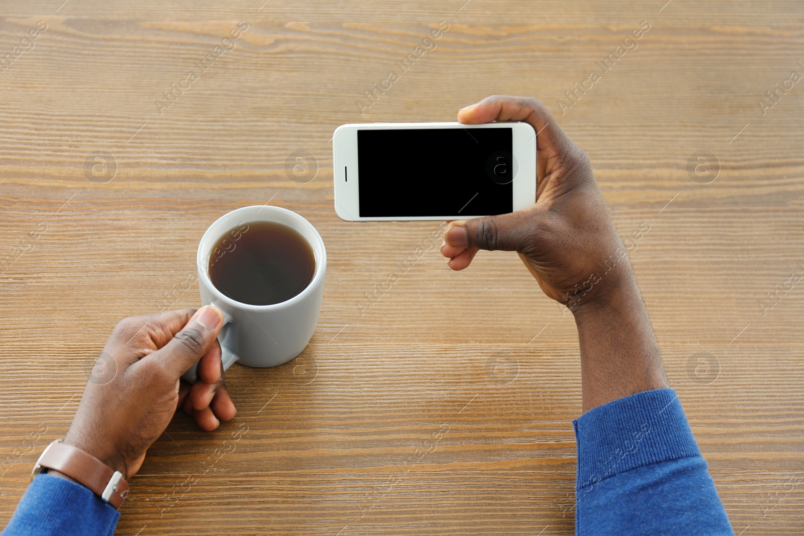 Photo of African-American man holding mobile phone with blank screen in hand at table