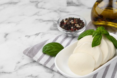 Photo of Plate with tasty mozzarella slices and basil leaves on white marble table. Space for text