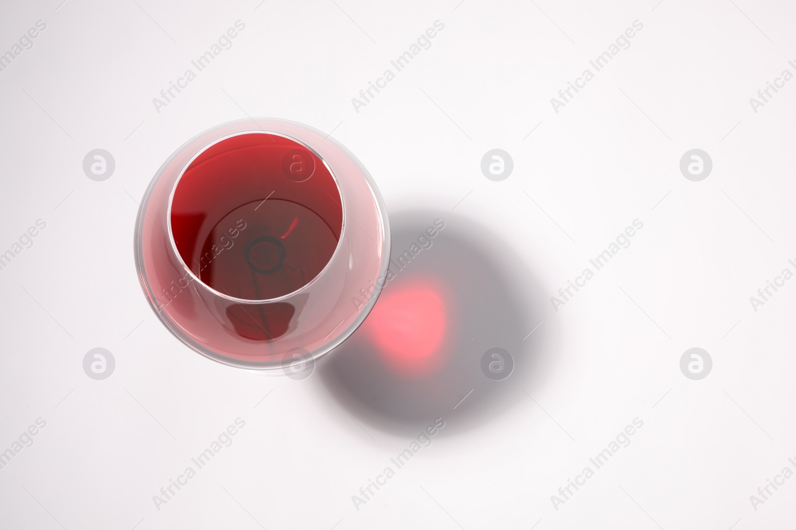 Photo of Red wine in glass and shadow on white background, top view. Space for text