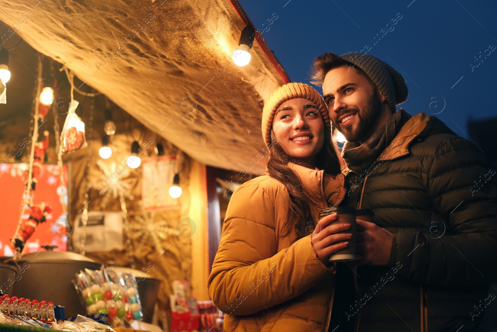 Photo of Lovely couple with cups of hot drinks spending time together at Christmas fair