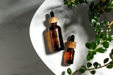 Glass bottles of essential oil and green plant on white table, flat lay. Space for text