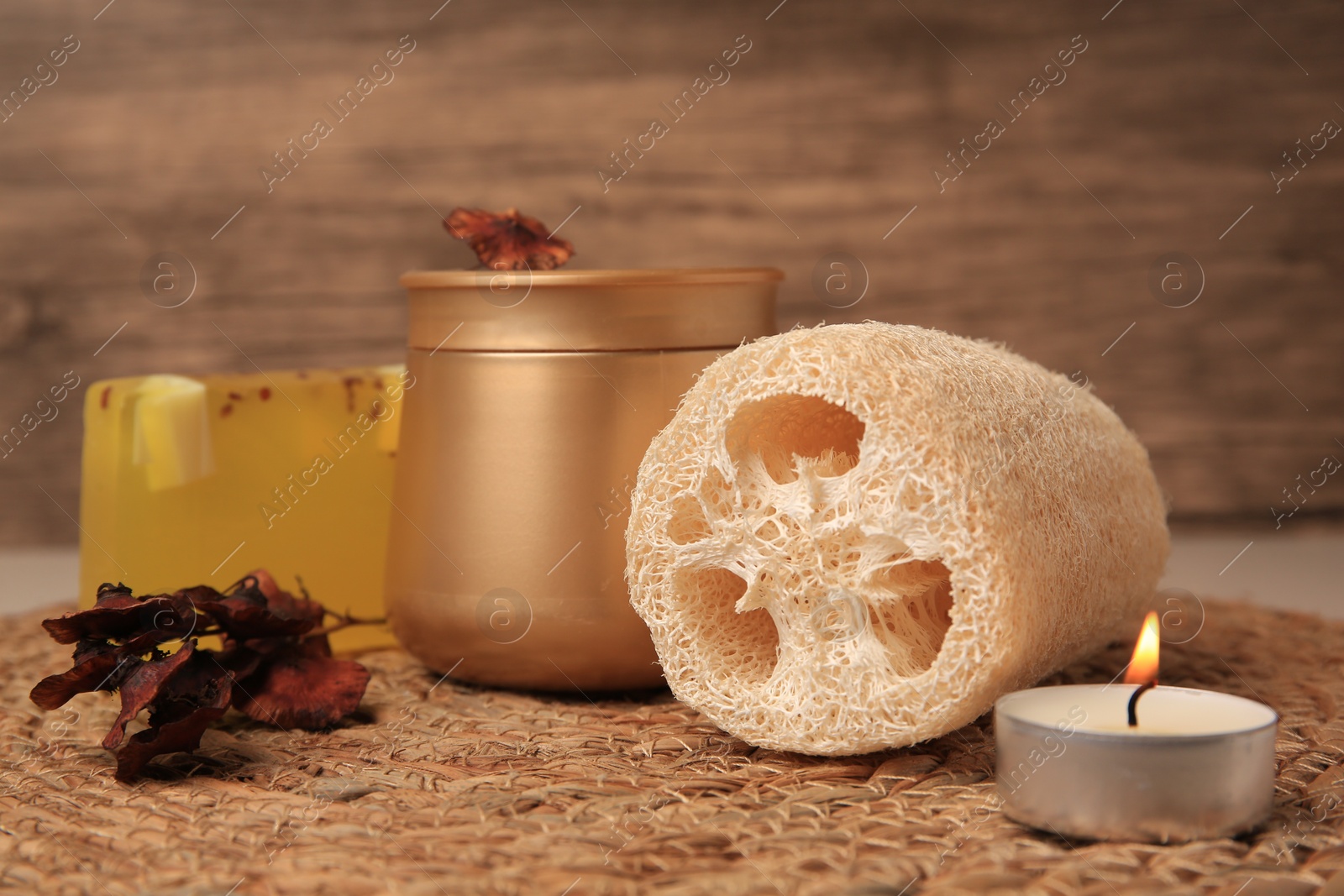 Photo of Natural loofah sponge, cosmetic products and candle on wicker mat, closeup