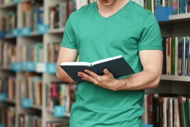 Young man with book near shelving unit in library, closeup