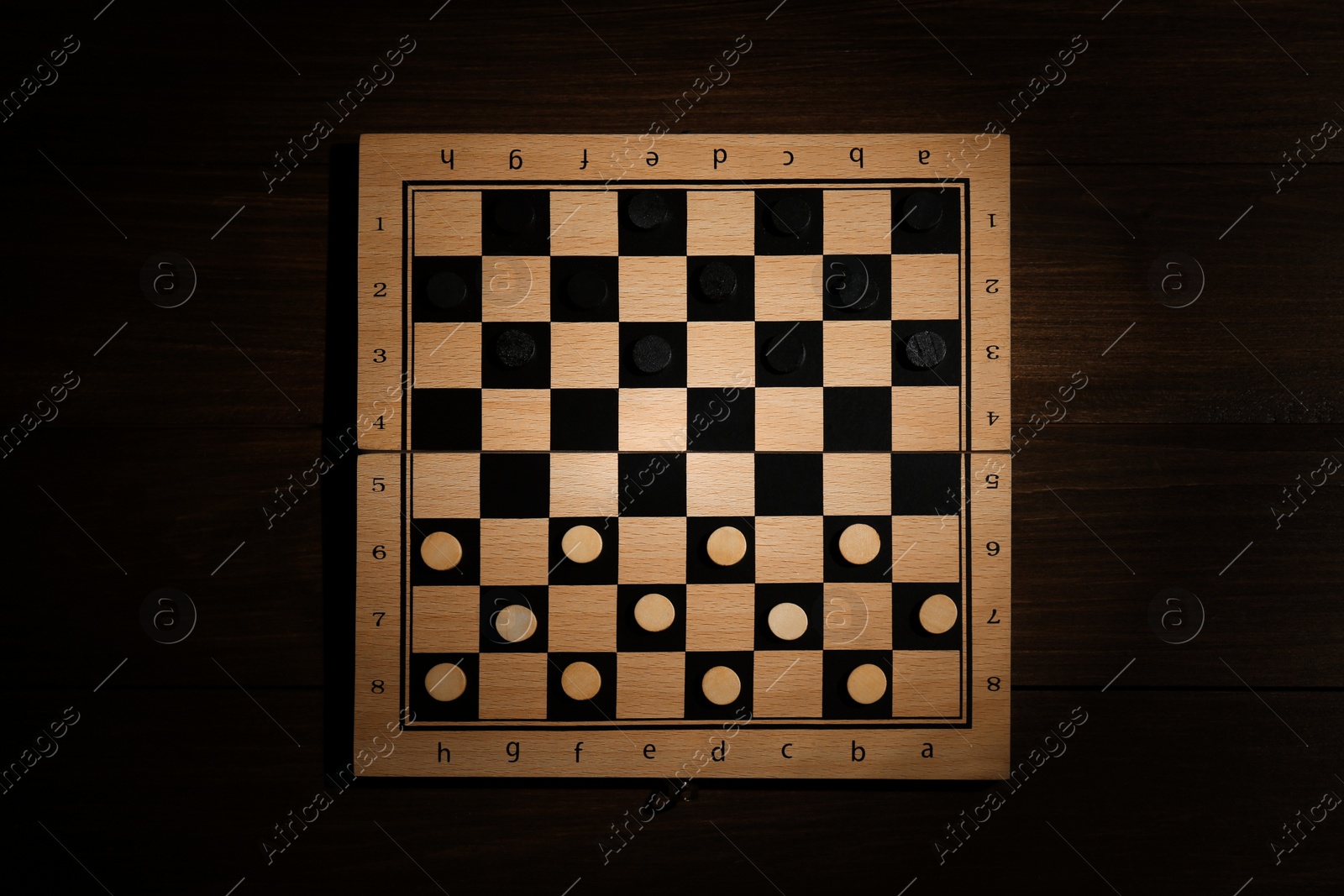 Photo of Checkerboard with game pieces on wooden table, top view