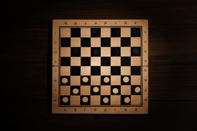 Photo of Checkerboard with game pieces on wooden table, top view