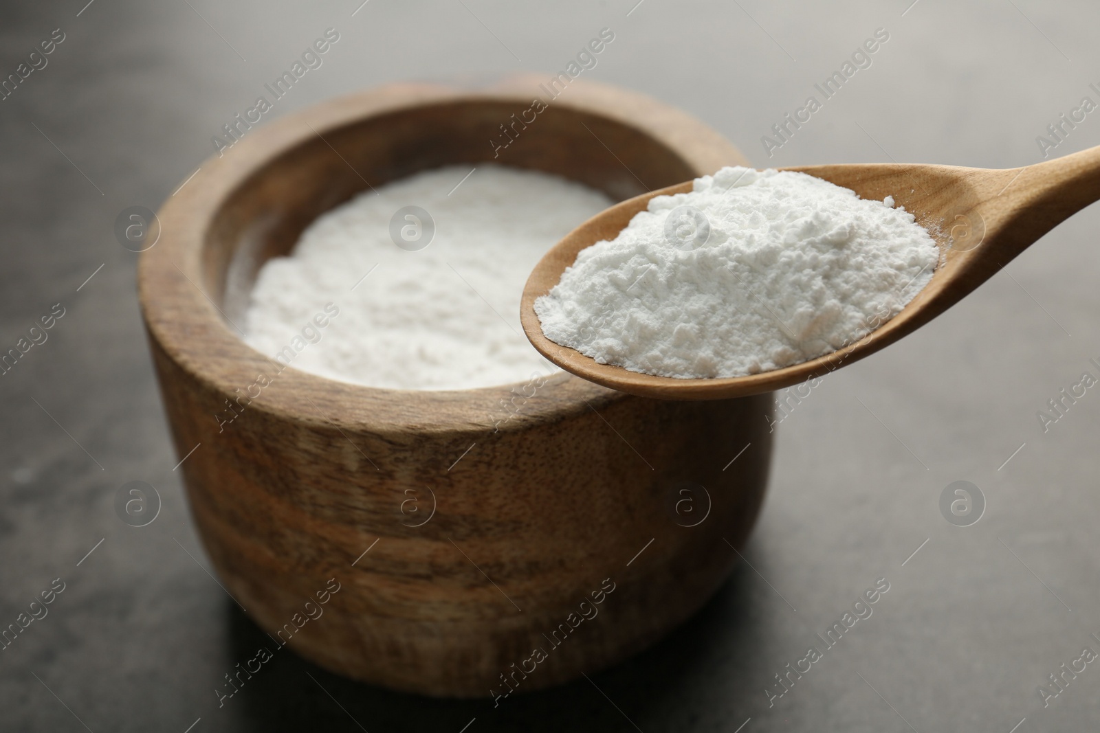 Photo of Spoon of baking powder over bowl at grey textured table, closeup. Space for text