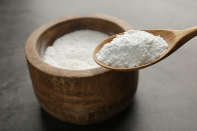 Spoon of baking powder over bowl at grey textured table, closeup. Space for text