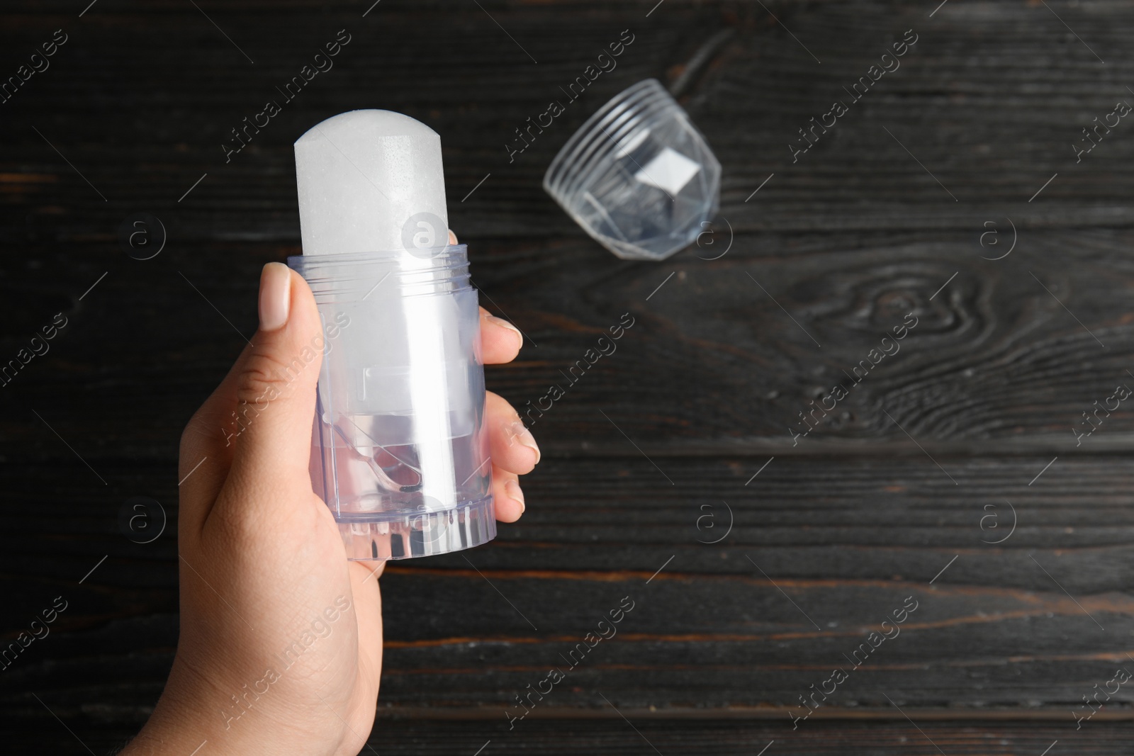 Photo of Young woman holding natural crystal alum deodorant over black wooden table, top view. Space for text