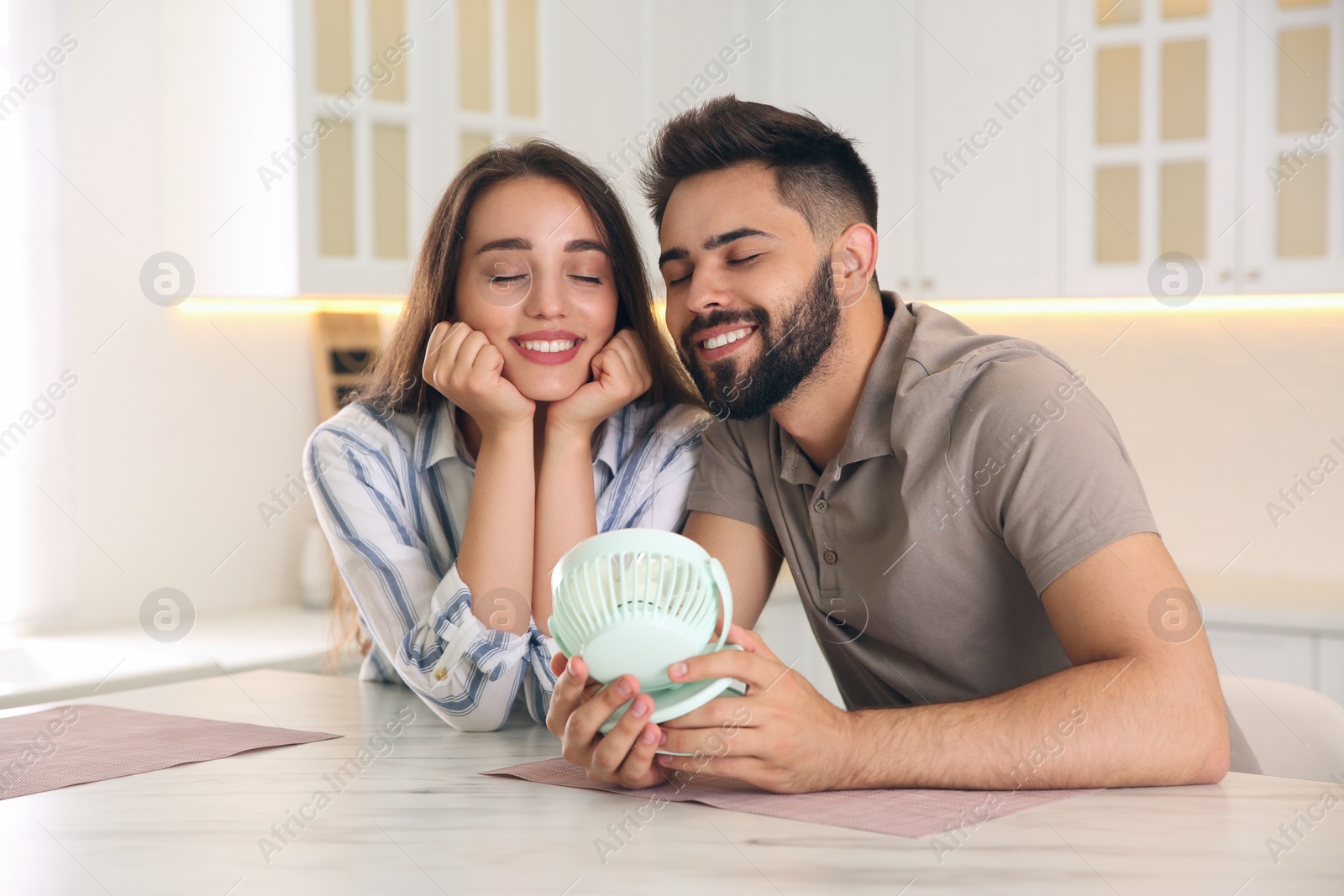 Photo of Couple enjoying air flow from portable fan at home. Summer heat