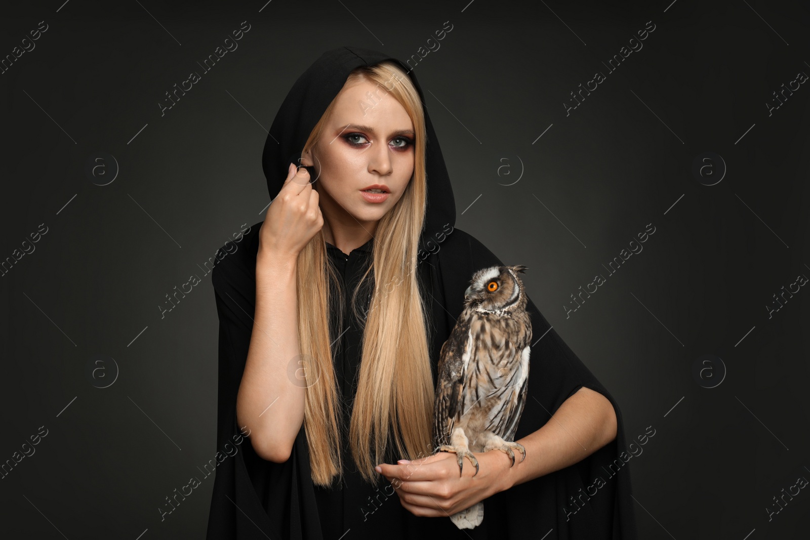 Photo of Witch in black mantle with owl on dark background. Scary fantasy character