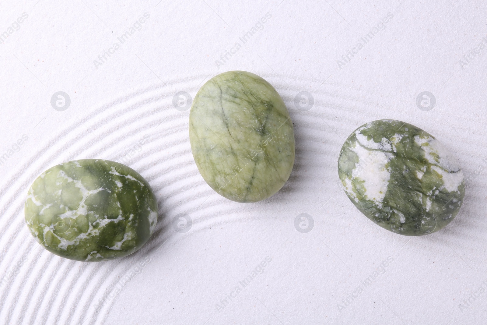 Photo of Zen garden stones on white sand with pattern, flat lay