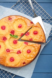 Delicious cut pineapple pie with cherry on blue wooden table, top view