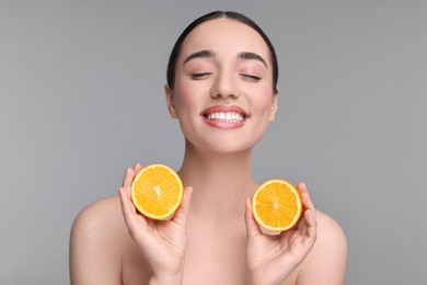 Photo of Beautiful young woman with pieces of orange on grey background