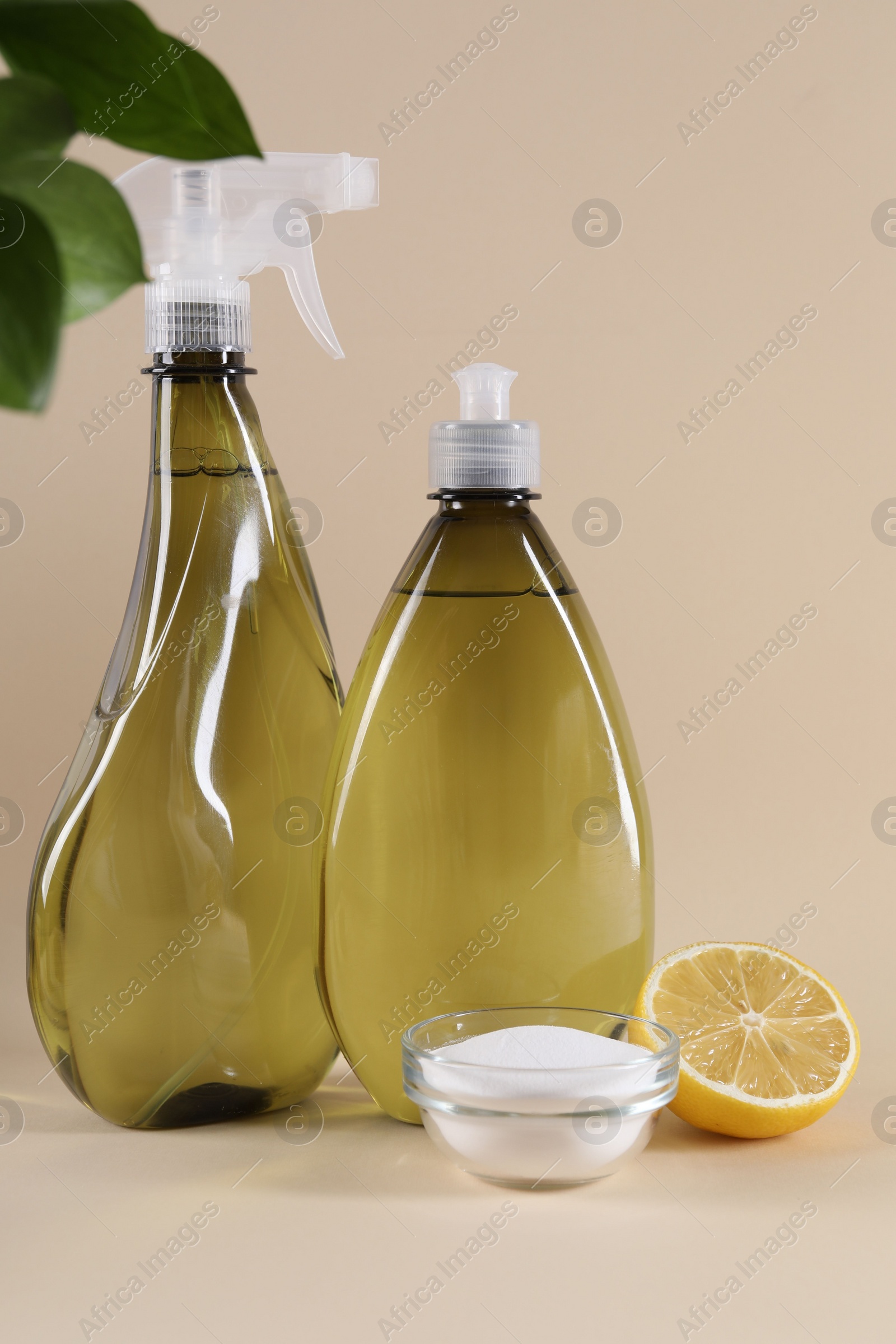 Photo of Bottles of cleaning product, lemon and baking soda on beige background