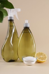 Bottles of cleaning product, lemon and baking soda on beige background