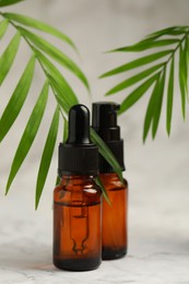 Bottles of organic cosmetic products and green leaves on light background