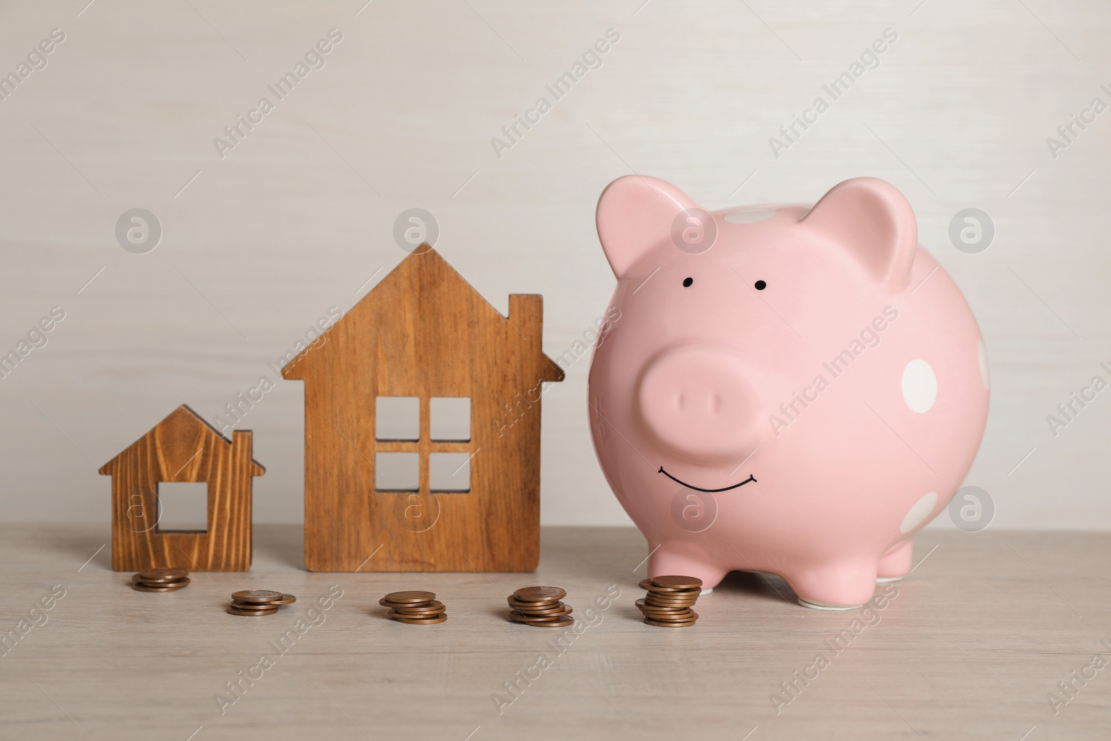 Photo of Piggy bank, stacked coins and house models on white wooden table