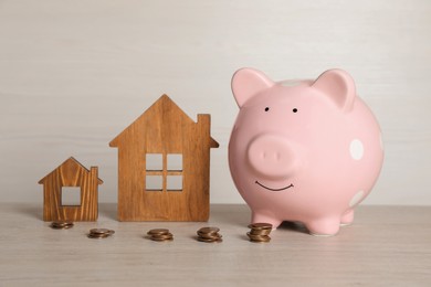 Photo of Piggy bank, stacked coins and house models on white wooden table