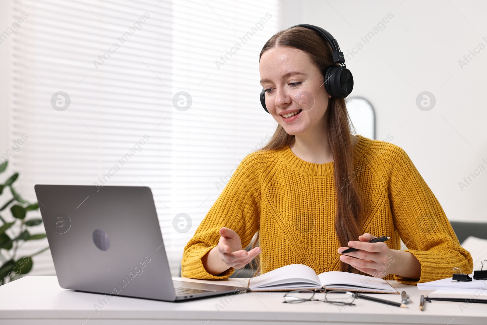 Photo of E-learning. Young woman using laptop during online lesson at white table indoors