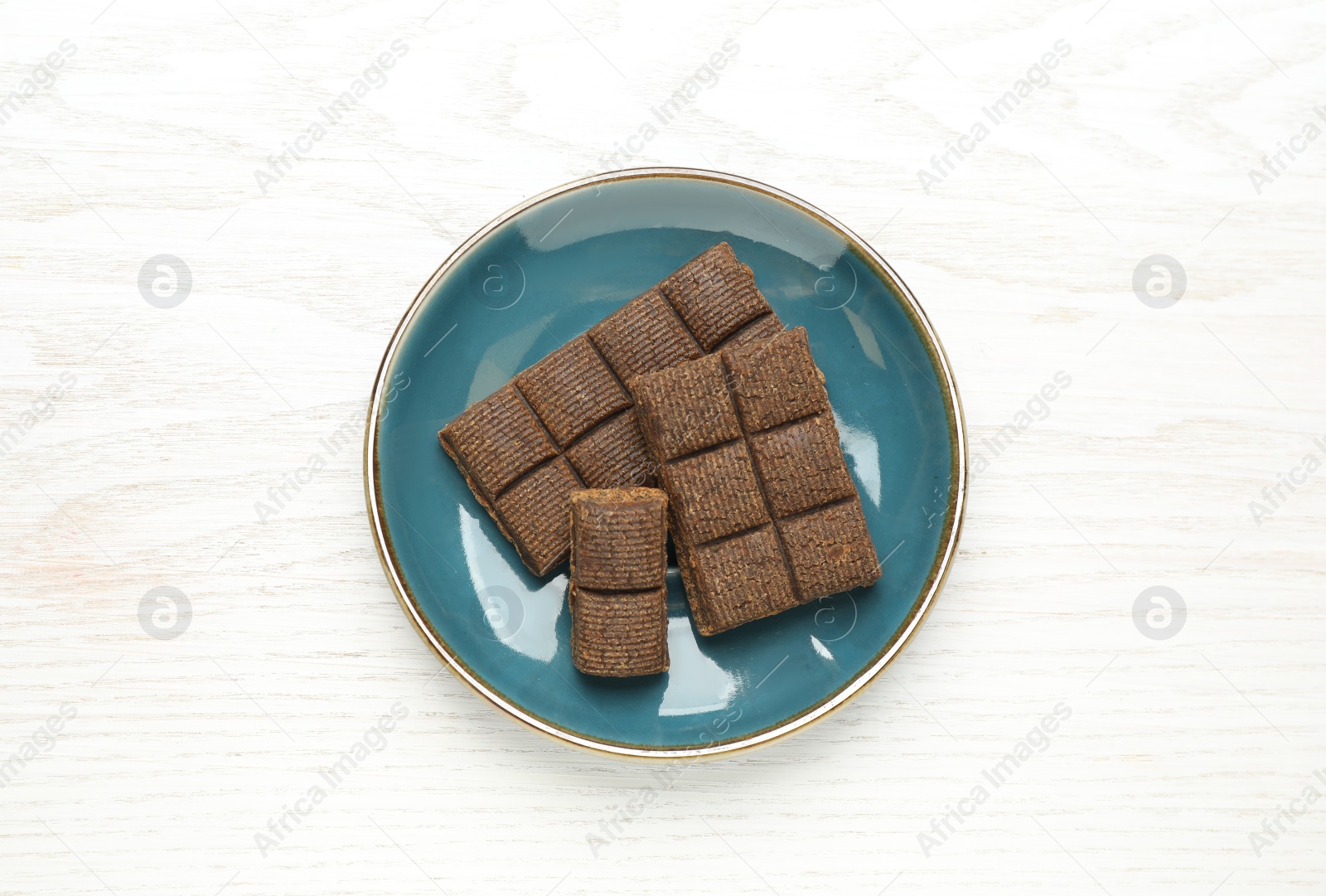 Photo of Blue plate with delicious and healthy hematogen on white wooden table, top view