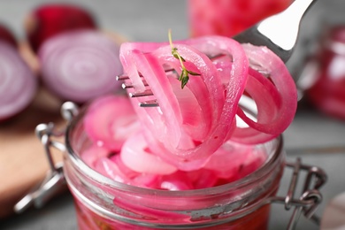 Photo of Fork with tasty pickled onion slices over jar on table, closeup