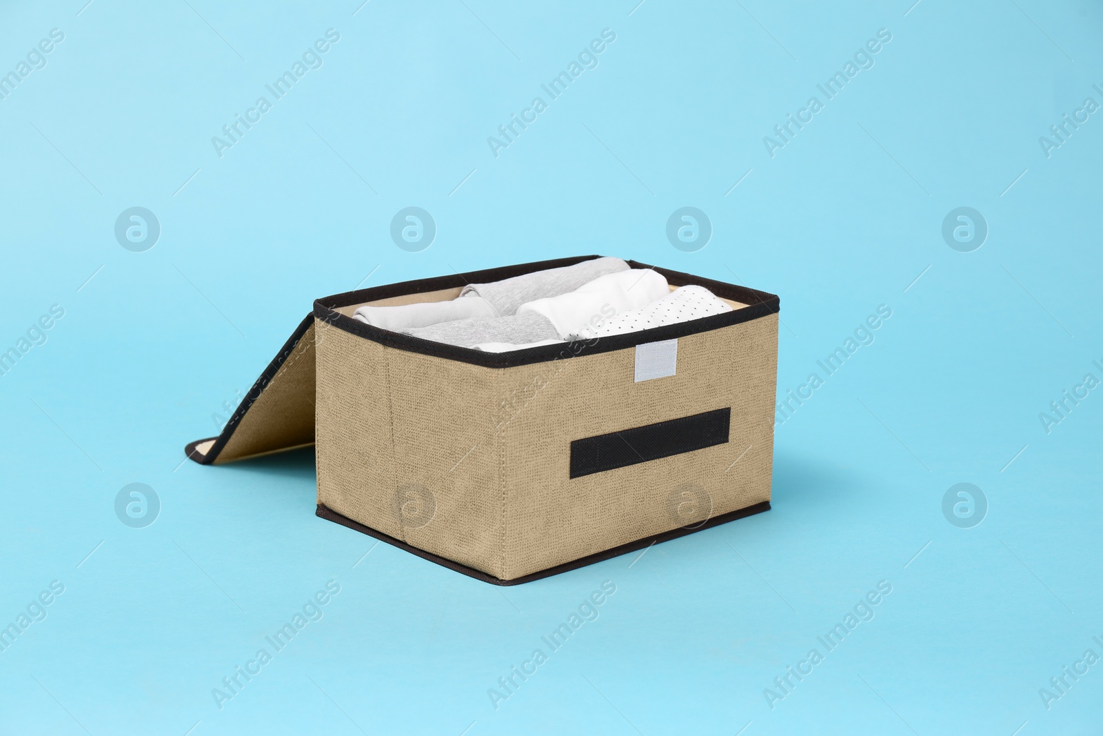 Photo of Textile storage case with folded clothes on light blue background