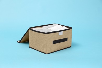 Photo of Textile storage case with folded clothes on light blue background