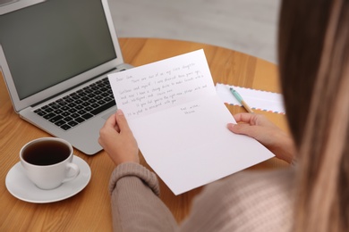 Woman reading letter at wooden table indoors, closeup