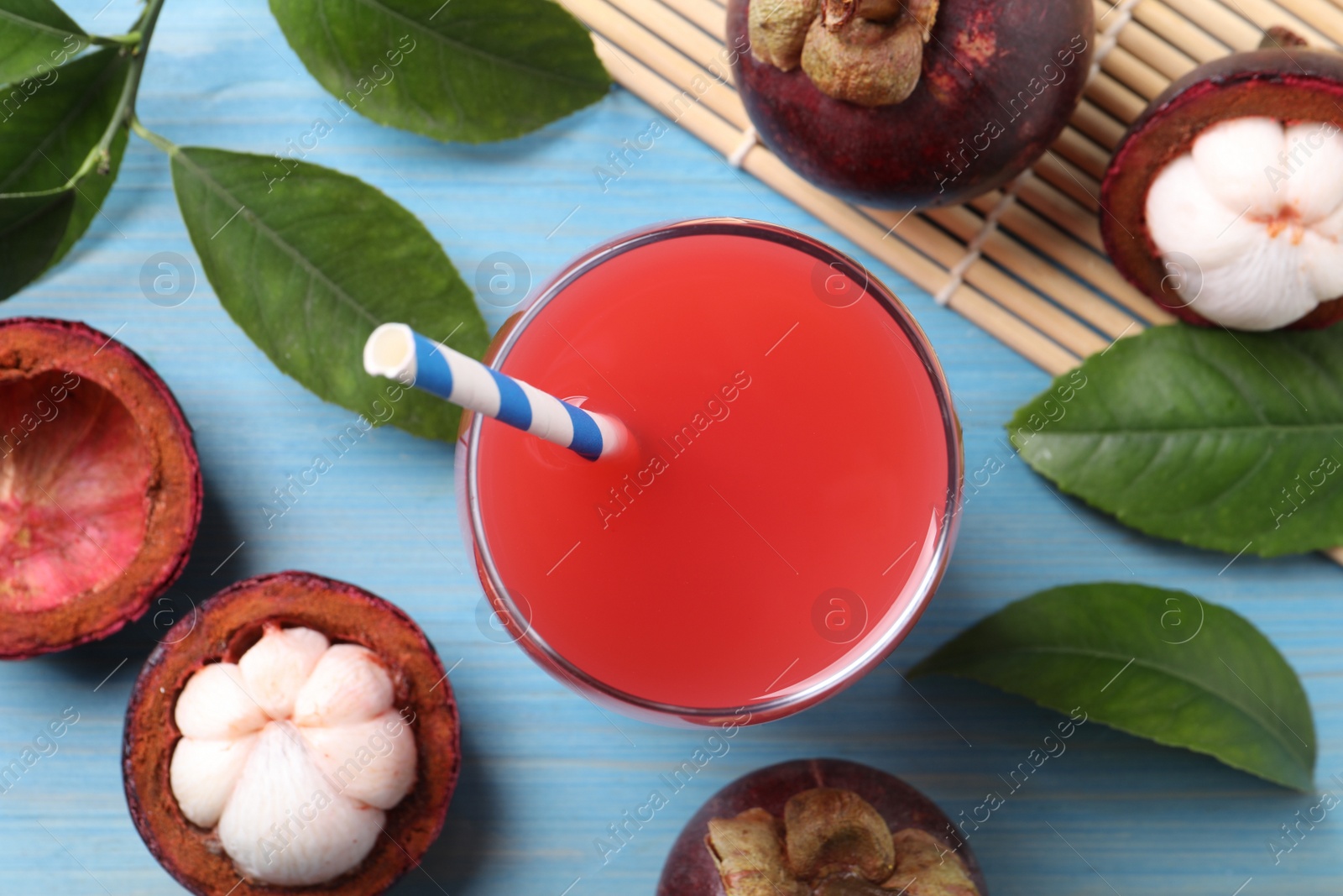 Photo of Delicious fresh mangosteen juice in glass on light blue wooden table, flat lay