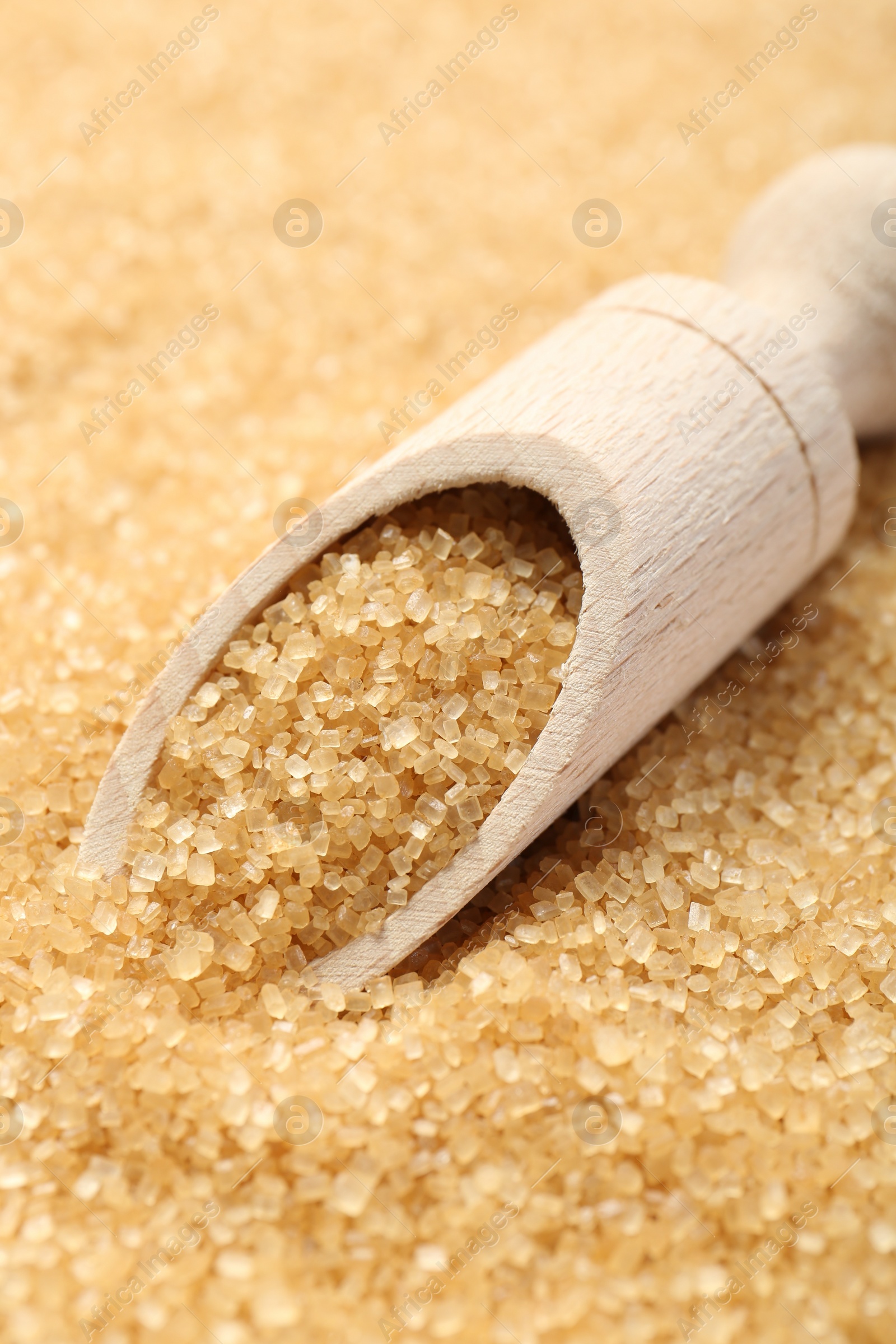 Photo of Wooden scoop on granulated brown sugar, closeup view