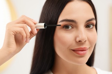 Photo of Beautiful woman applying serum onto her eyelashes indoors, closeup. Cosmetic product
