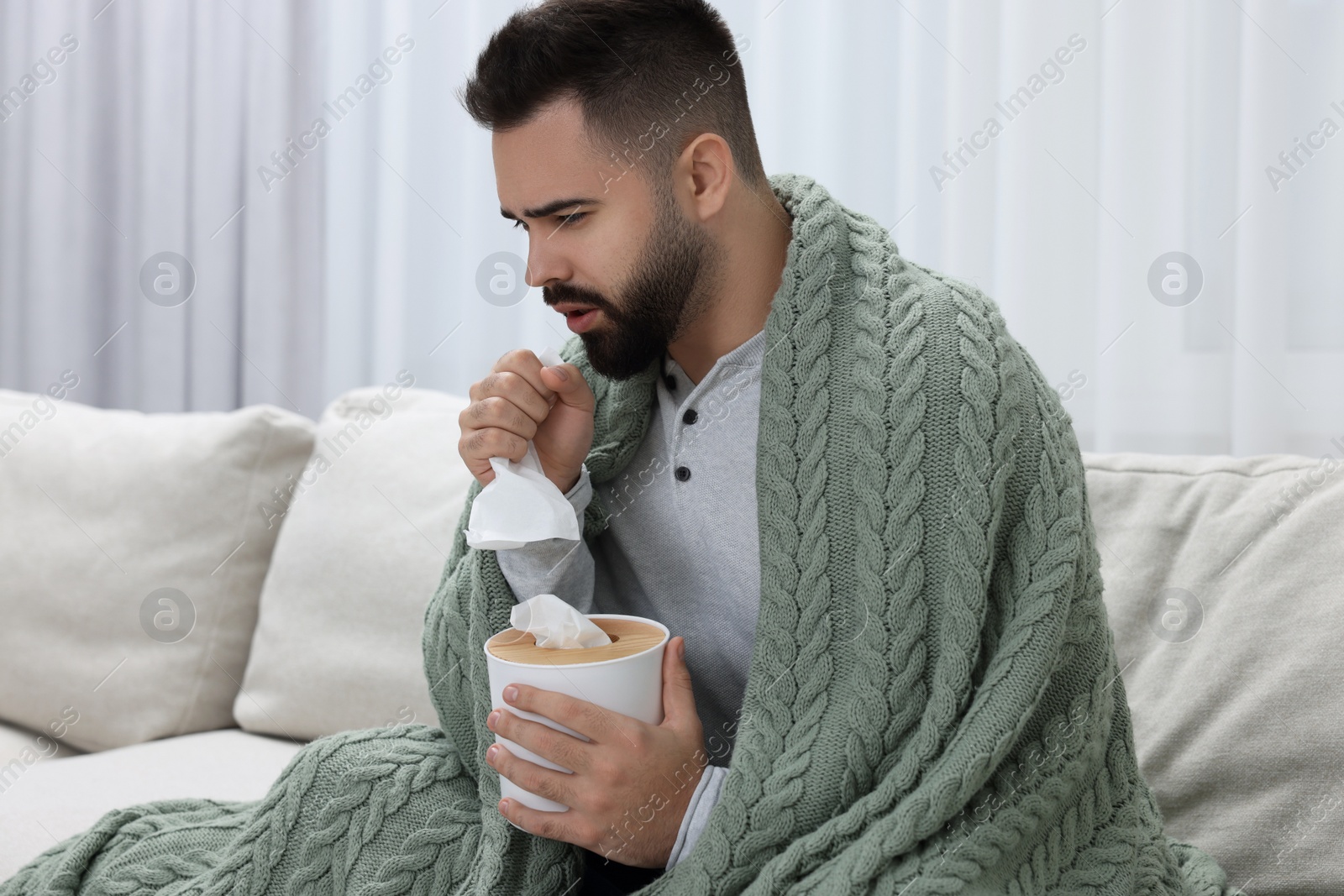 Photo of Sick man with tissue coughing at home