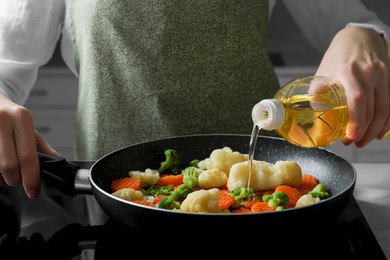 Photo of Woman pouring cooking oil from bottle into frying pan with vegetables on stove, closeup