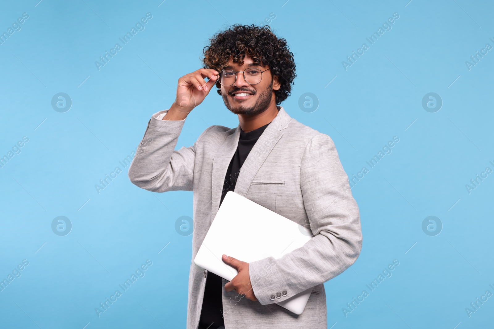 Photo of Smiling man with laptop on light blue background. Space for text