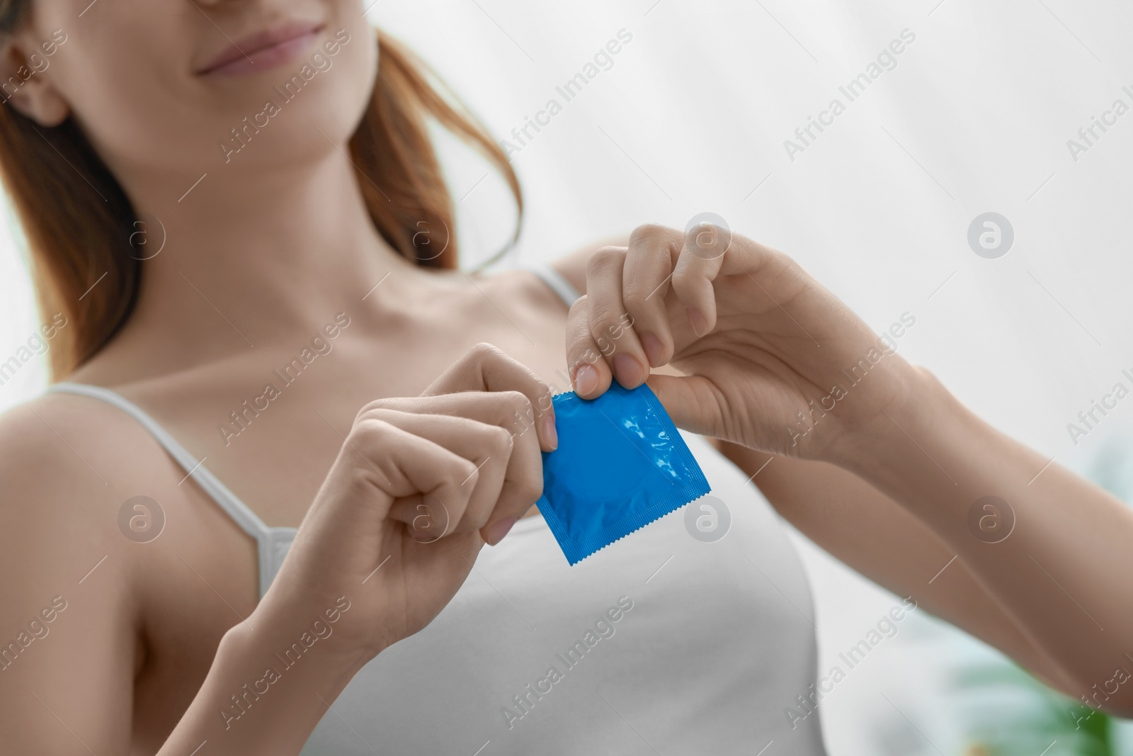 Photo of Woman opening condom indoors, closeup. Safe sex