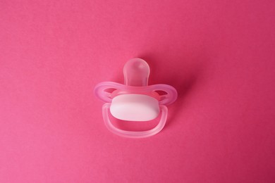 Photo of One baby pacifier on pink background, above view