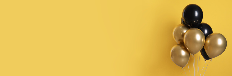 Image of Bunch of black and gold balloons on yellow background, space for text. Banner design 