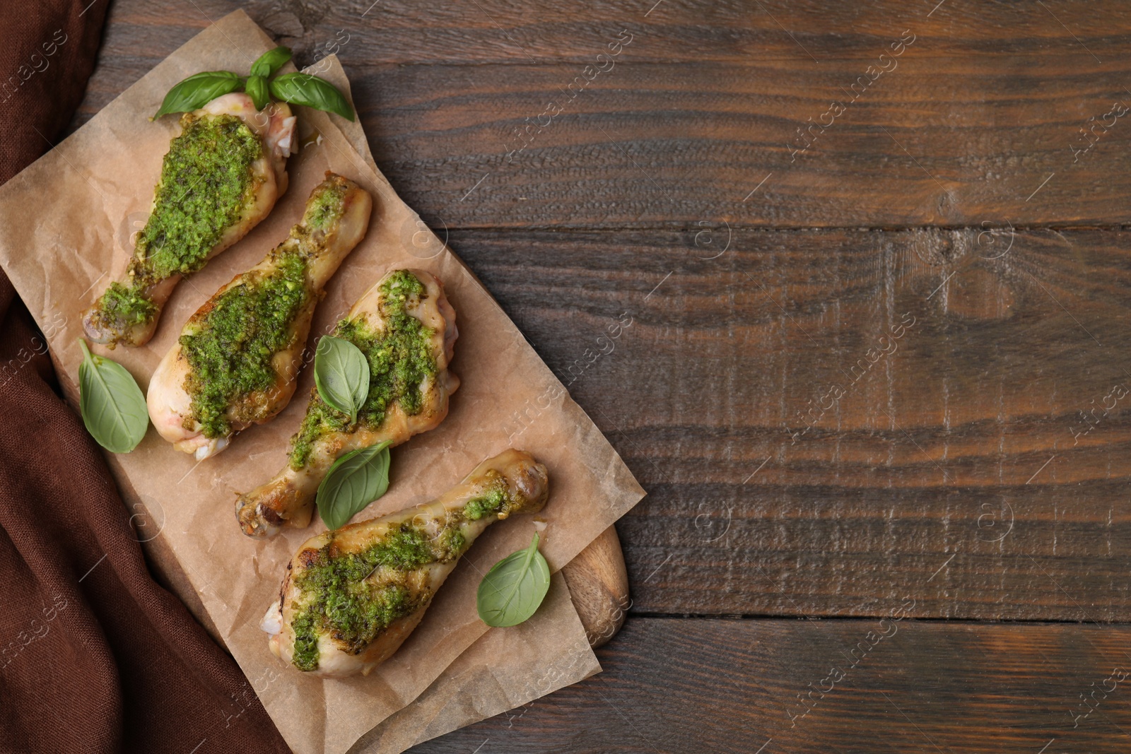 Photo of Delicious fried chicken drumsticks with pesto sauce and basil on wooden table, top view. Space for text