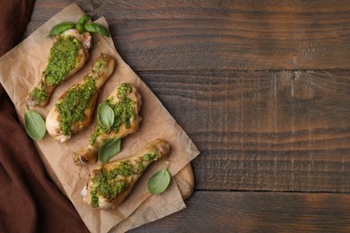 Delicious fried chicken drumsticks with pesto sauce and basil on wooden table, top view. Space for text