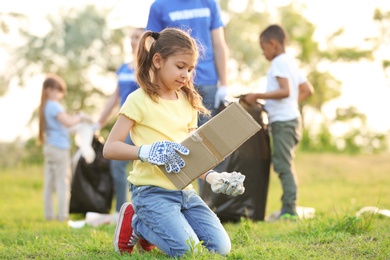 Photo of Little girl collecting trash in park. Volunteer project