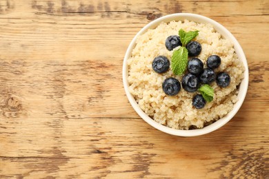 Photo of Tasty quinoa porridge with blueberries and mint in bowl on wooden table, top view. Space for text